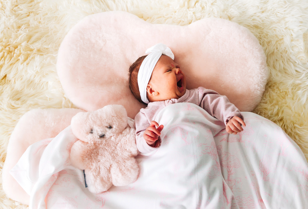 A baby and a pink teddy bear and baby rug